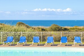 A poolside area with six blue lounge chairs and a white fence. - Résidence Lagrange Vacances L'Estran (Les Sables-d'Olonne)