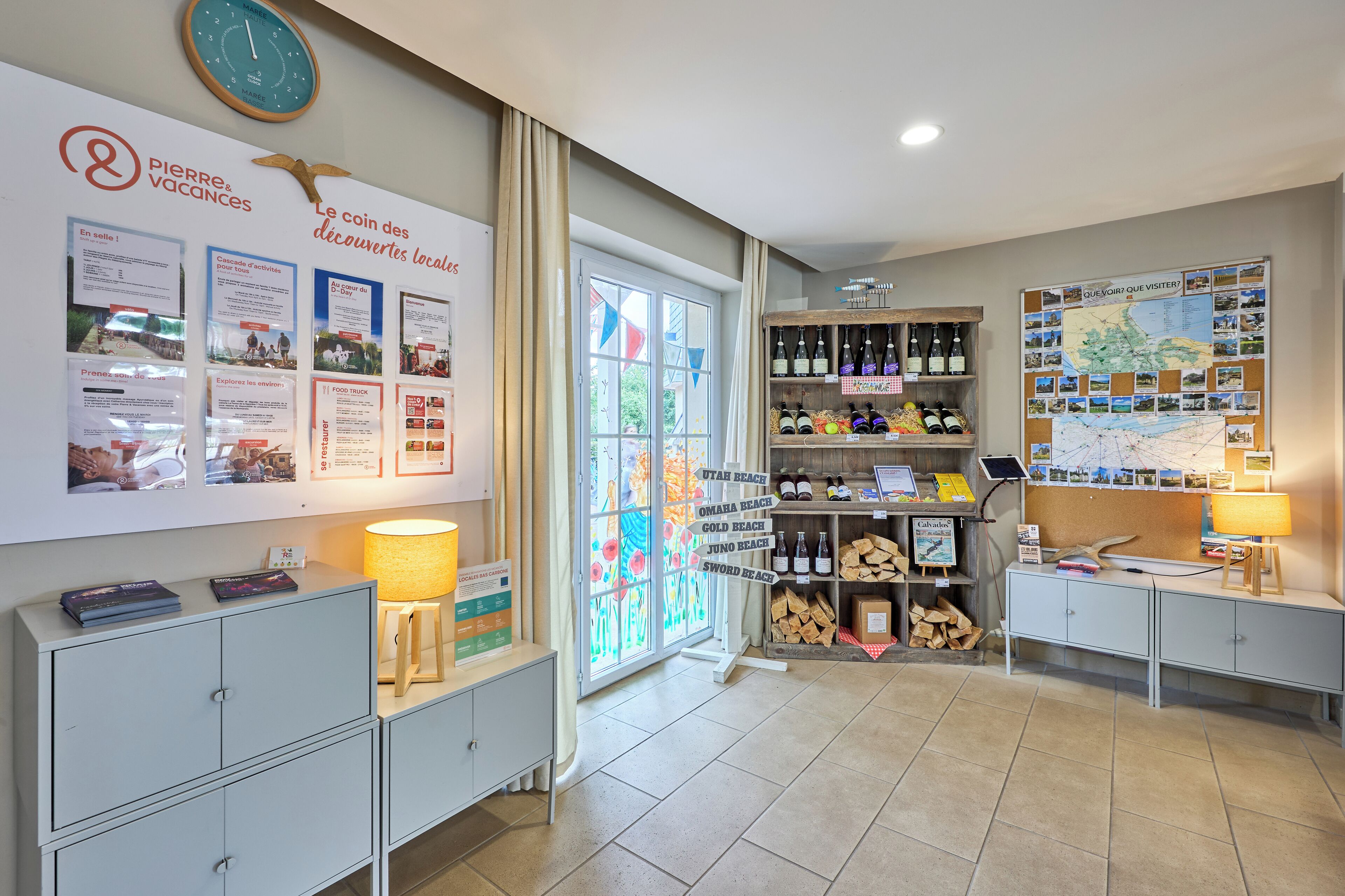 A hotel reception area with a whiteboard displaying local attractions, a wooden desk with a lamp, a wine rack, and a bulletin board with a map.