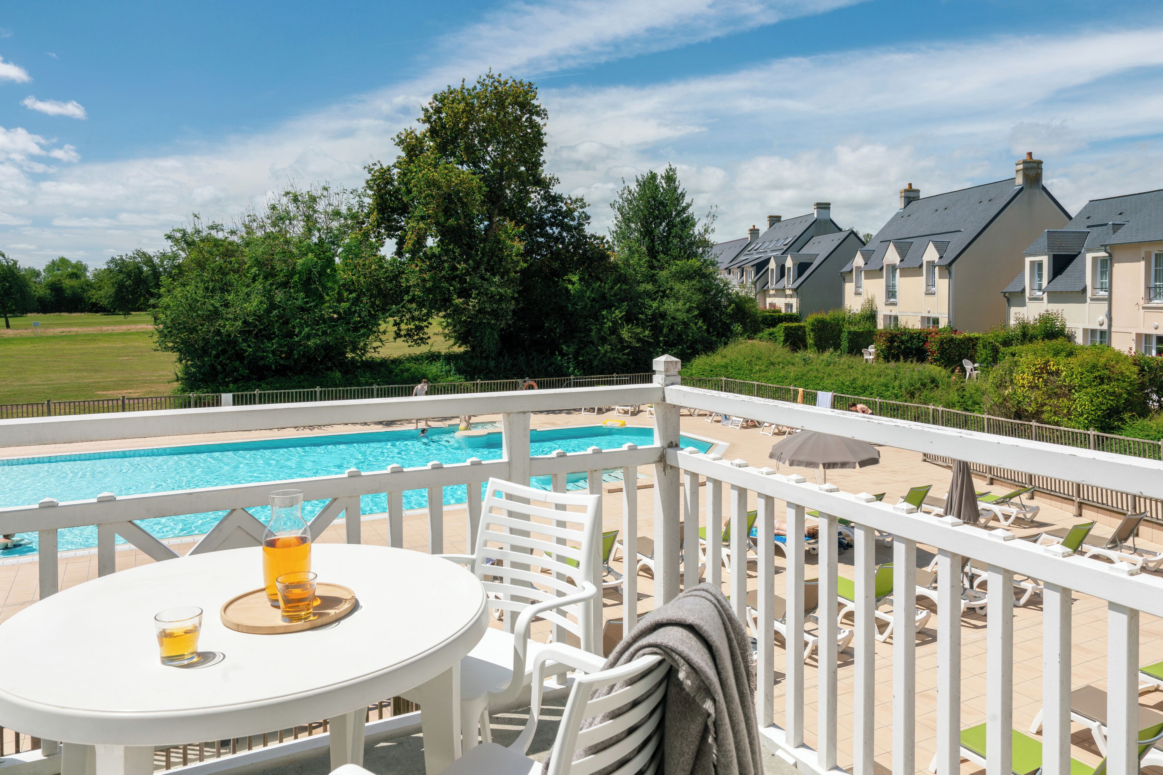 Zona de piscina con mesa, sillas y vistas a una piscina y casas.
