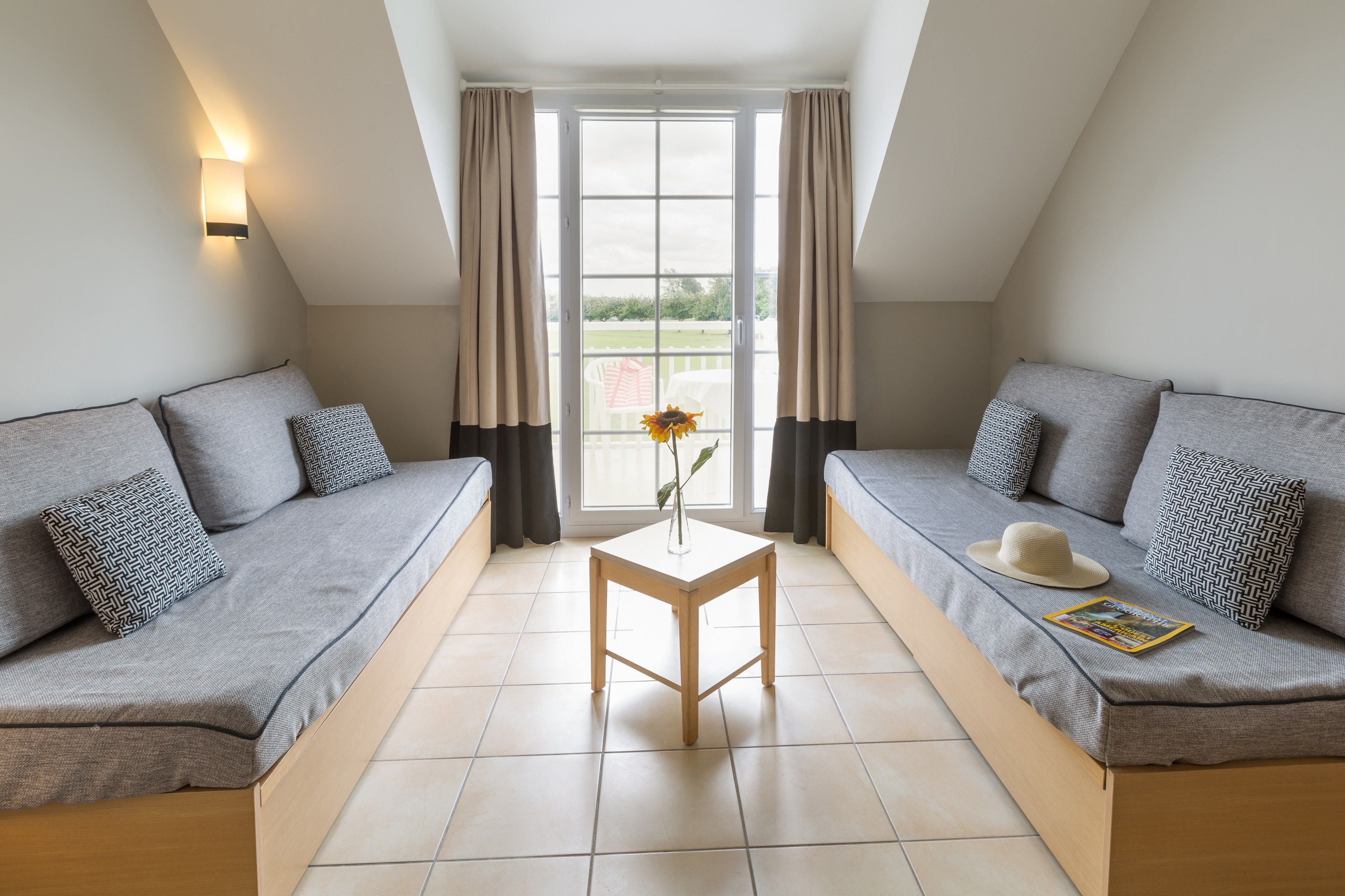 Una habitación moderna y bien iluminada con dos sofás grises, una mesita de madera y una ventana con cortinas.