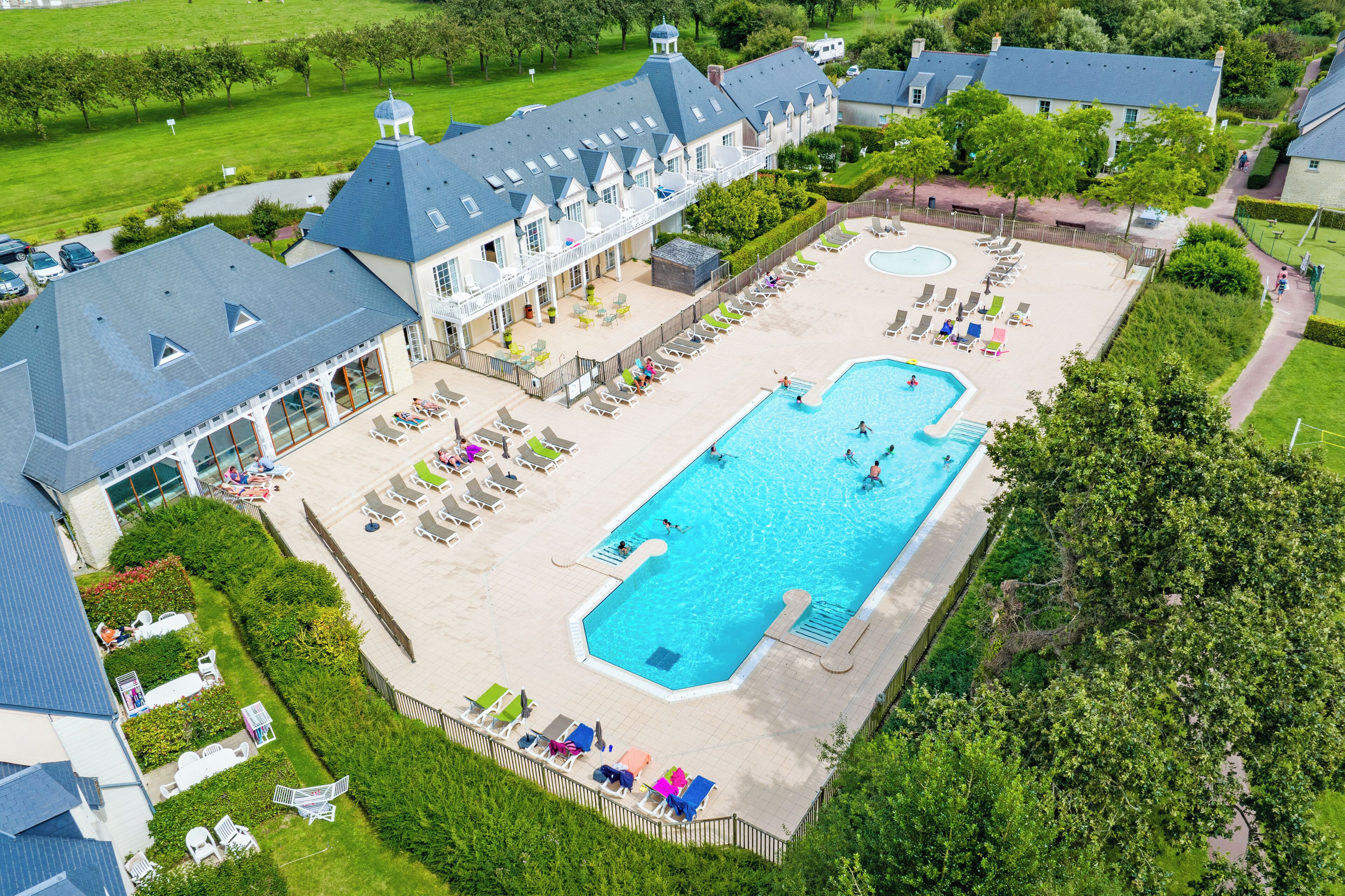 A large swimming pool surrounded by lounge chairs and a building with a balcony.