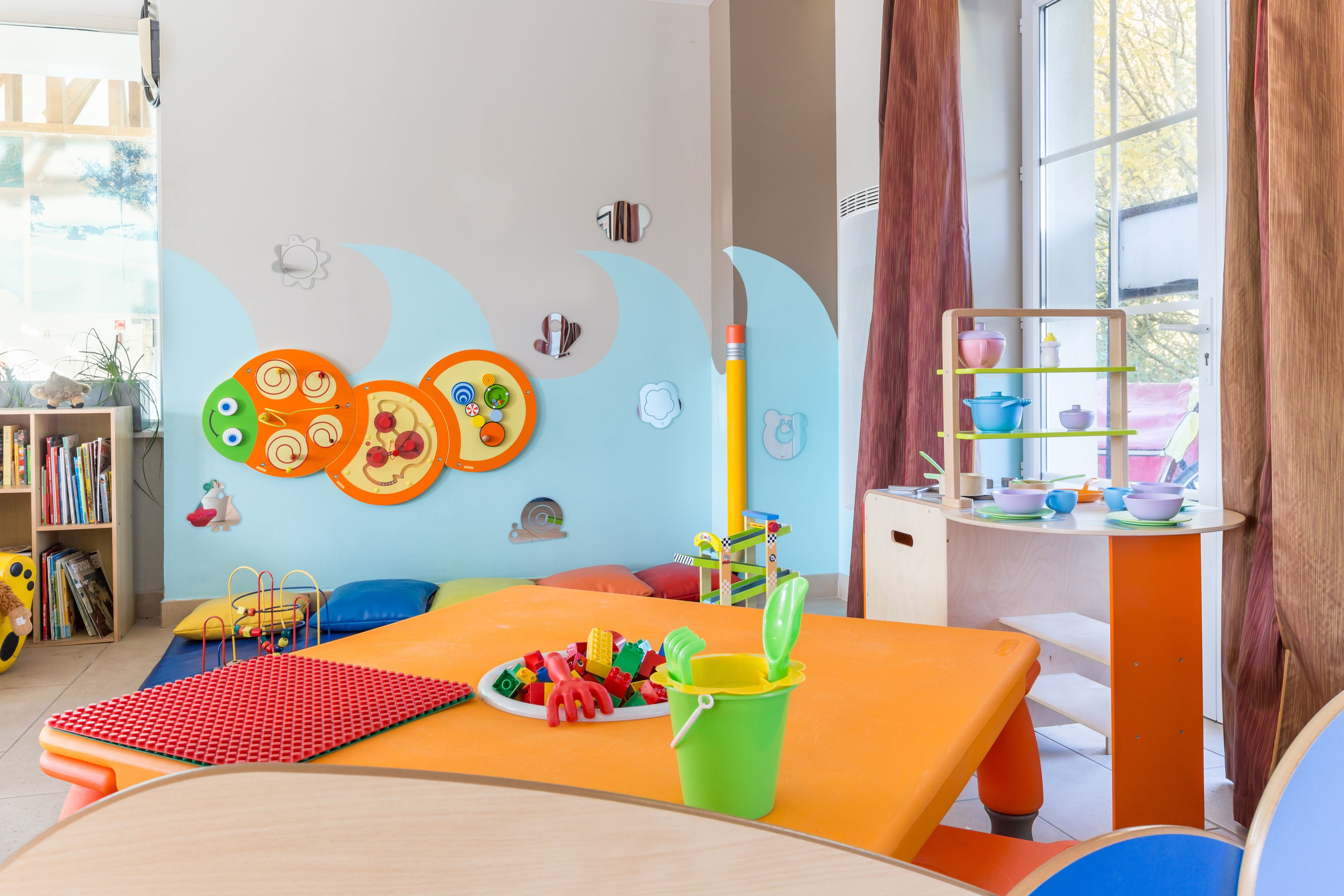 Une salle de jeux pour enfants aux couleurs vives, avec une table, des jouets et une bibliothèque.