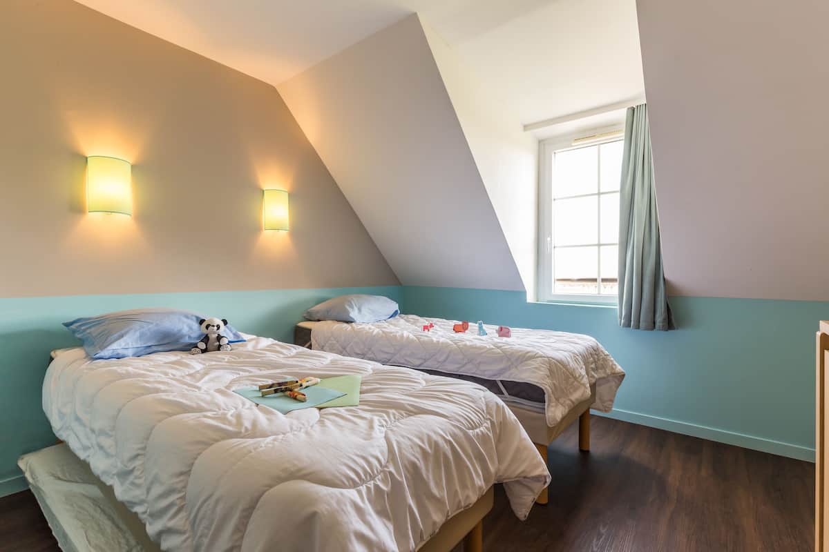 A bedroom with two beds, a window with curtains, and wall-mounted lighting.