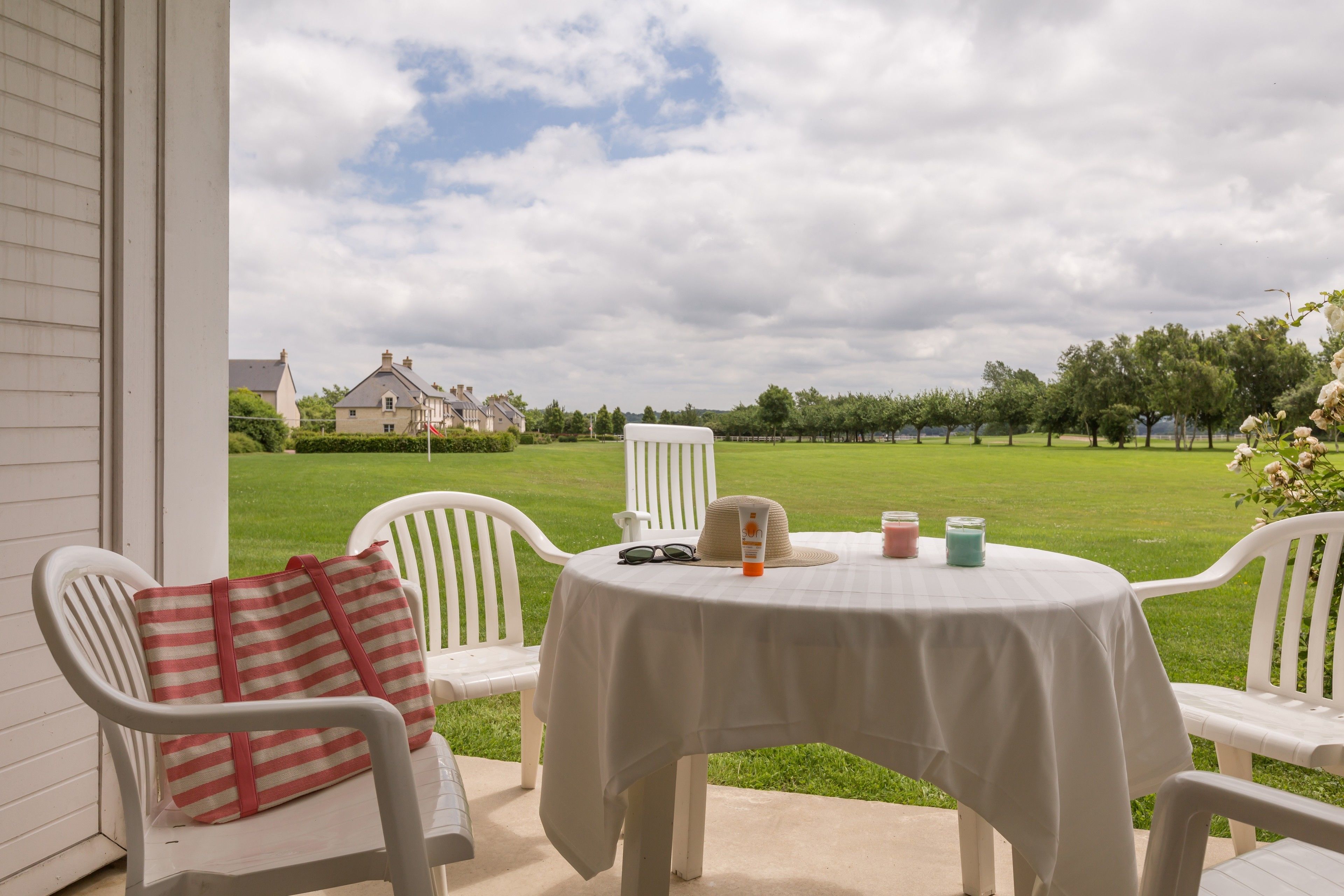 Eine Terrasse mit Tisch für zwei Personen, weißen Stühlen und einer Streifen-Tasche.