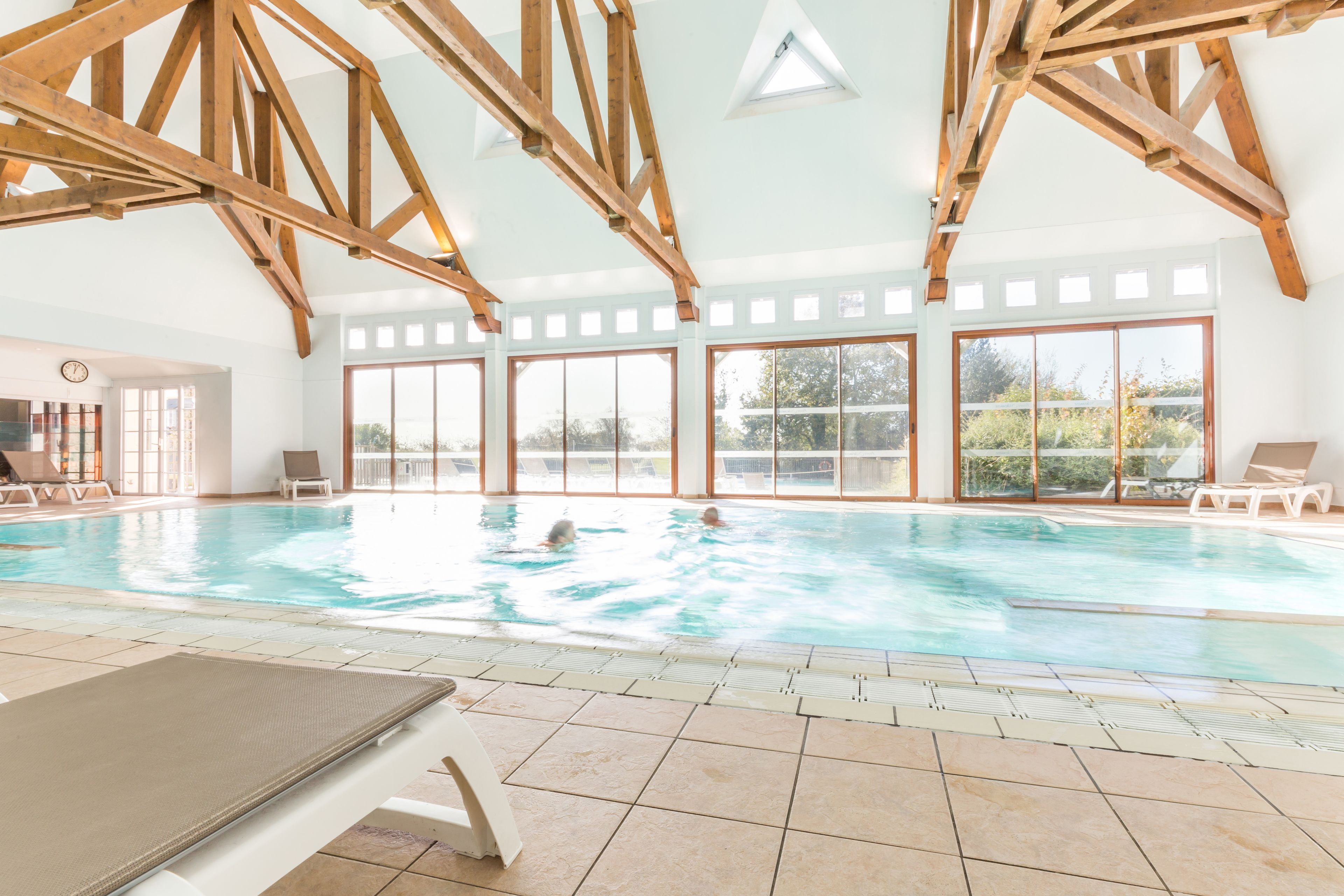 Ein Hallenbad mit Holzbalken, großen Fenstern und Liegestühlen.