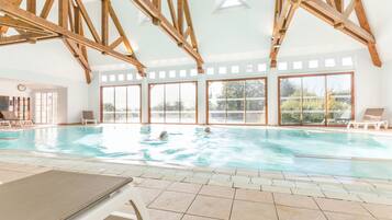Ein Hallenbad mit Holzbalken, großen Fenstern und Liegestühlen.