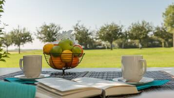Una mesa con una cesta de frutas, dos tazas y un libro abierto.