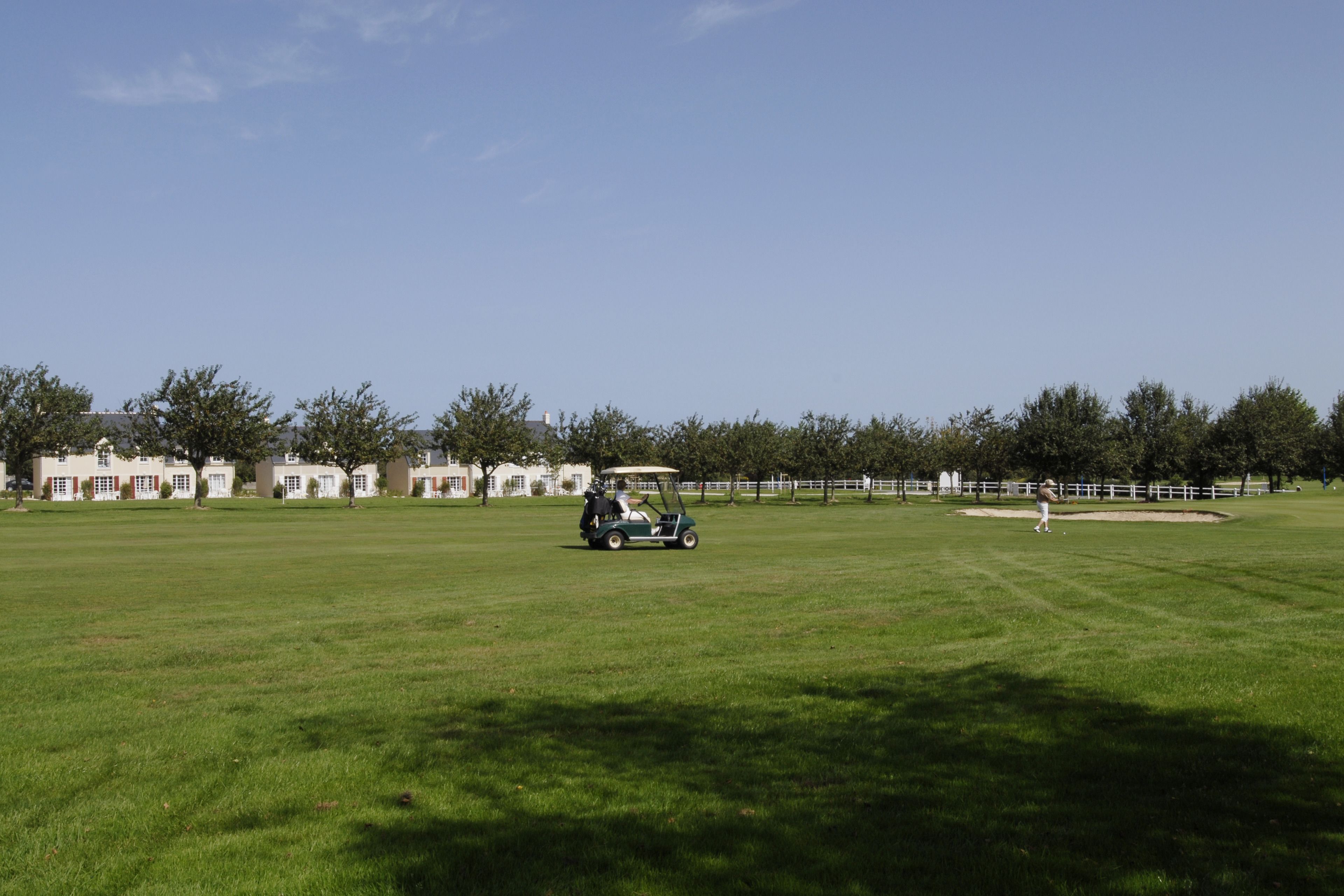 Un terrain de golf avec un gazon verdoyant, un chariot de golf et une personne au loin.