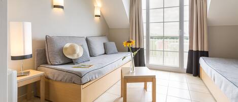 A modern bedroom with a sofa bed, a small wooden table, and a view of the outdoors through a large window.