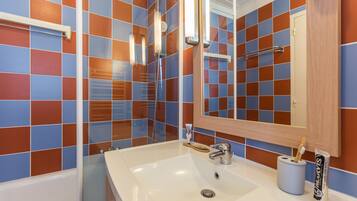 Une salle de bain avec un lavabo blanc, un miroir et un espace douche.