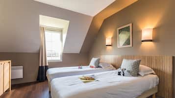 A hotel room with two beds, a window with curtains, a wall-mounted artwork, and a wall sconce.