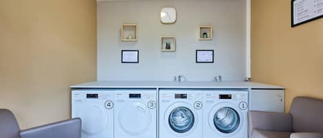 A laundry room with four washing machines, a clock, and framed certificates on the wall.