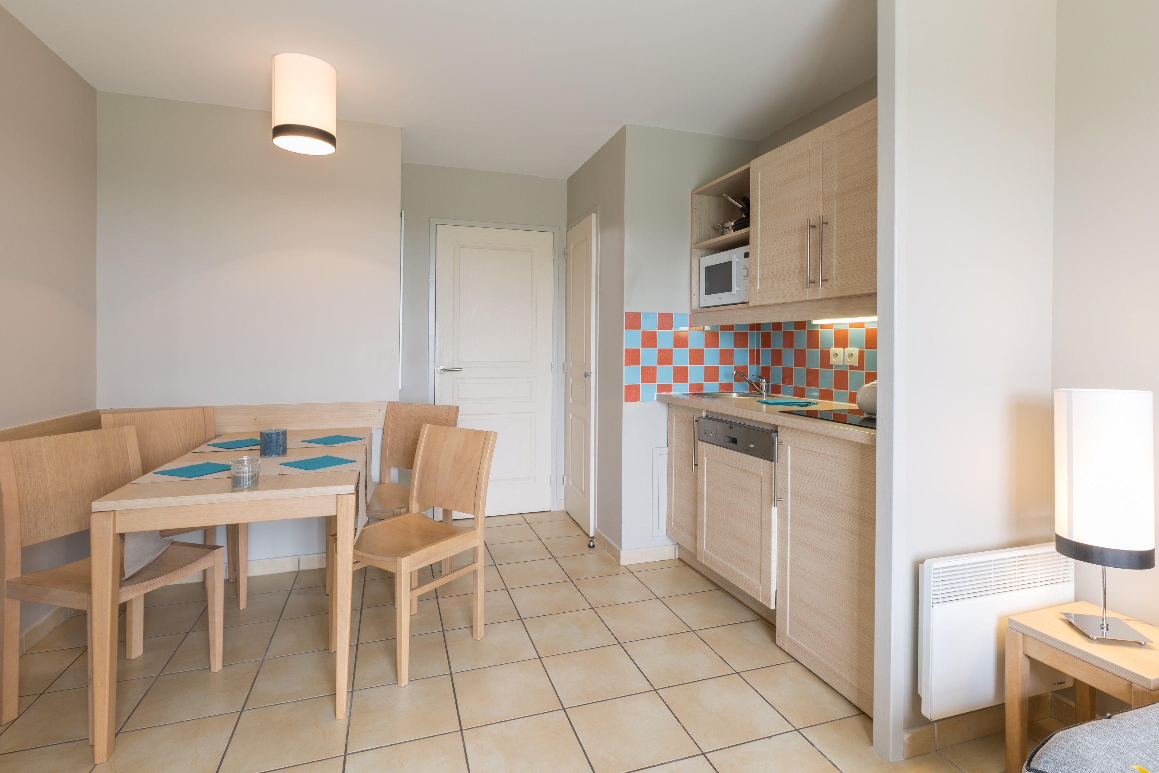 A compact kitchen with a dining area, featuring a microwave, oven, and tiled backsplash.