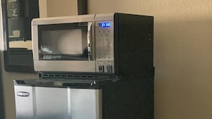 Un petit réfrigérateur, surmonté d’un four à micro-ondes, est placé dans un coin d’une pièce dont le sol est recouvert d’une moquette.