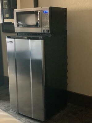 Un piccolo frigorifero con un forno a microonde sopra, posizionato in un angolo della stanza, che ha un pavimento con moquette.