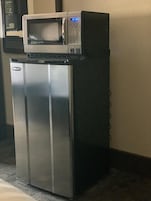 A compact refrigerator with a microwave on top, located in a corner of a room with a carpeted floor.