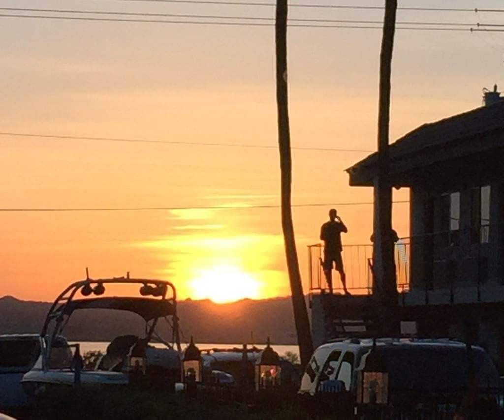 Ein Sonnenuntergang mit einer Person auf einem Balkon, einem Fahrzeug und einem Gebäude im Vordergrund.