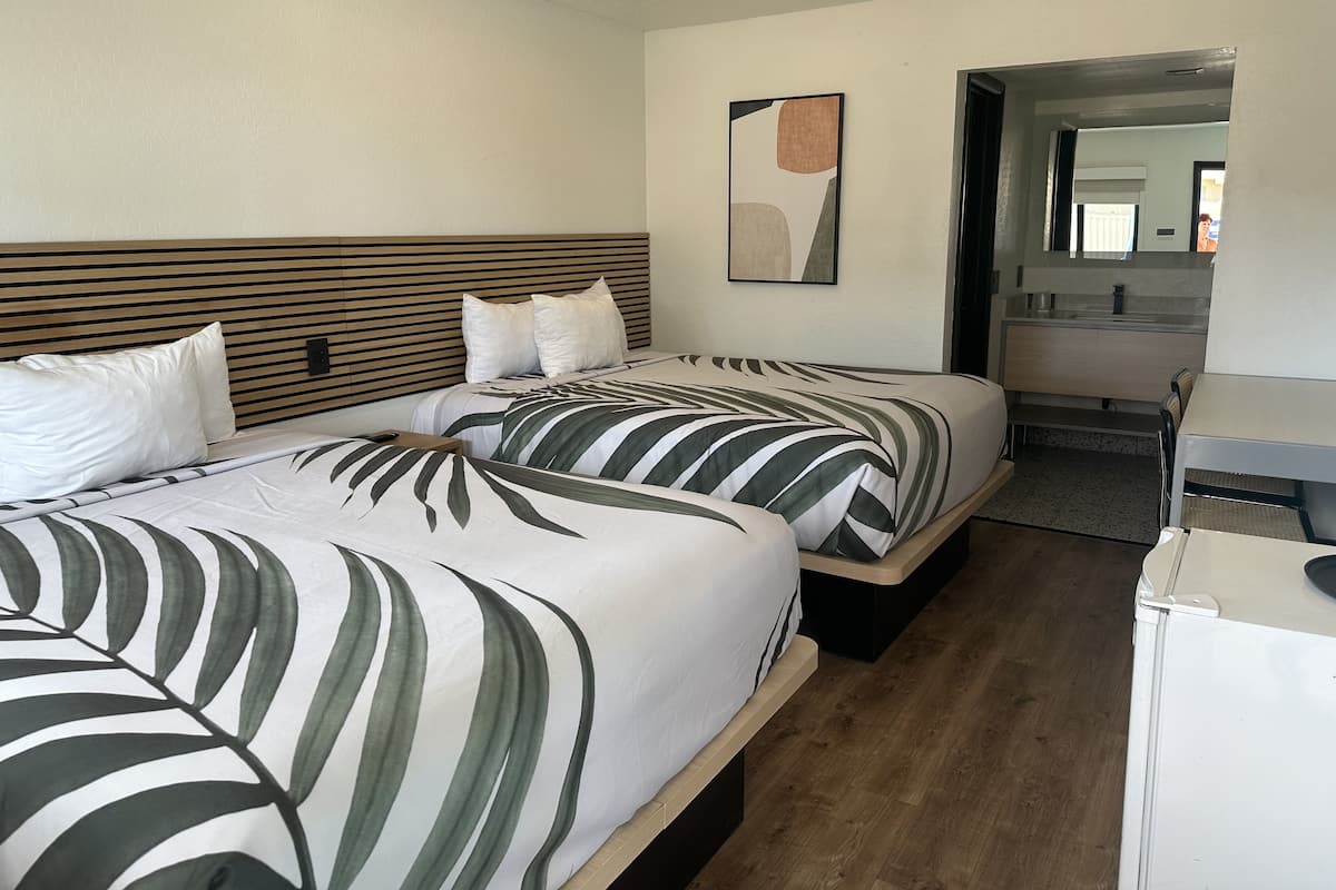 Una camera d'albergo con due letti, una testiera in legno, un quadro appeso al muro e una scrivania con una sedia.
