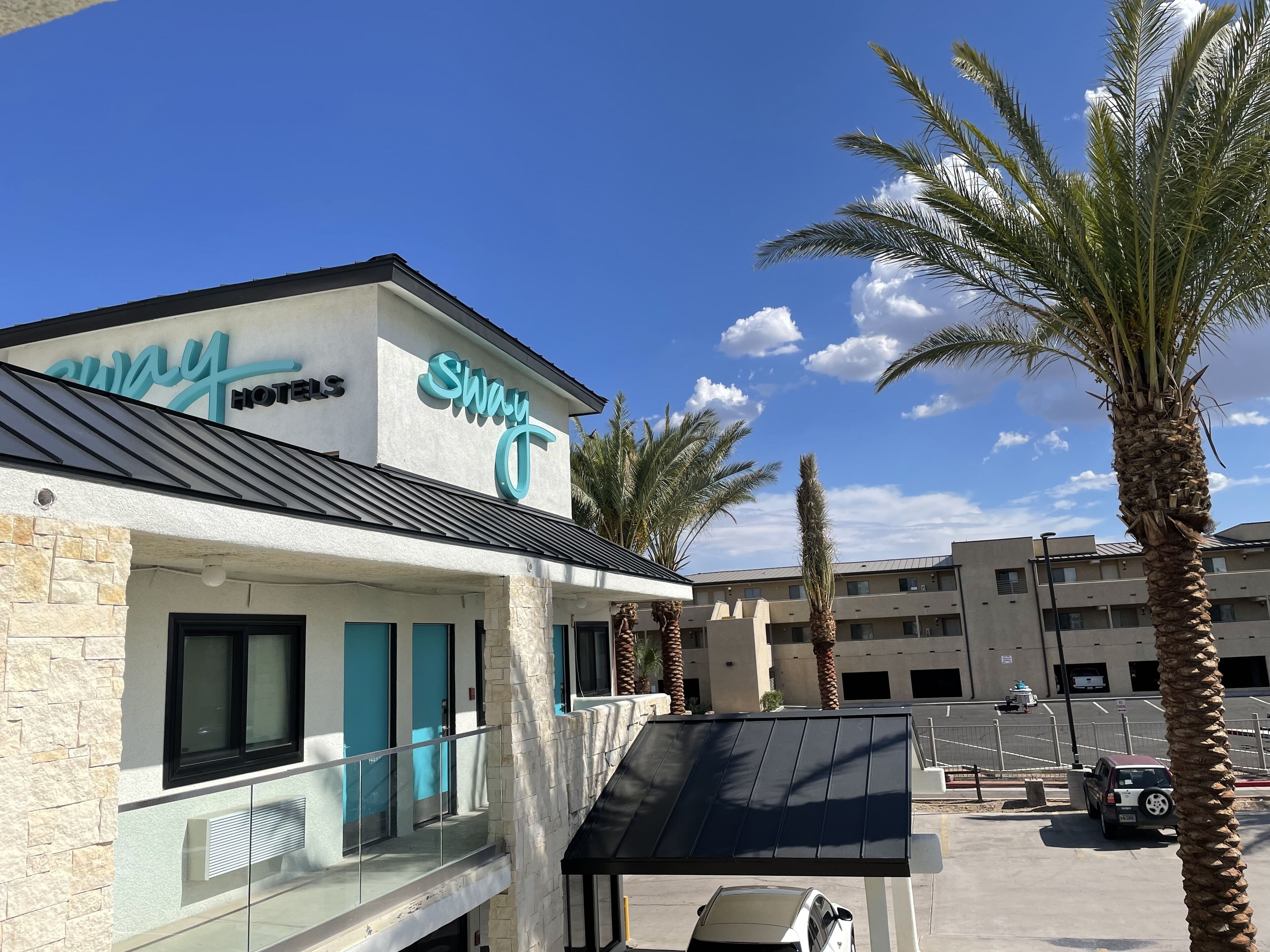 Un hotel con un letrero que dice "Sway Hotels" y un estacionamiento con algunos coches.