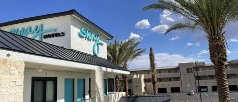 Un hotel con un letrero que dice "Sway Hotels" y un estacionamiento con algunos coches.