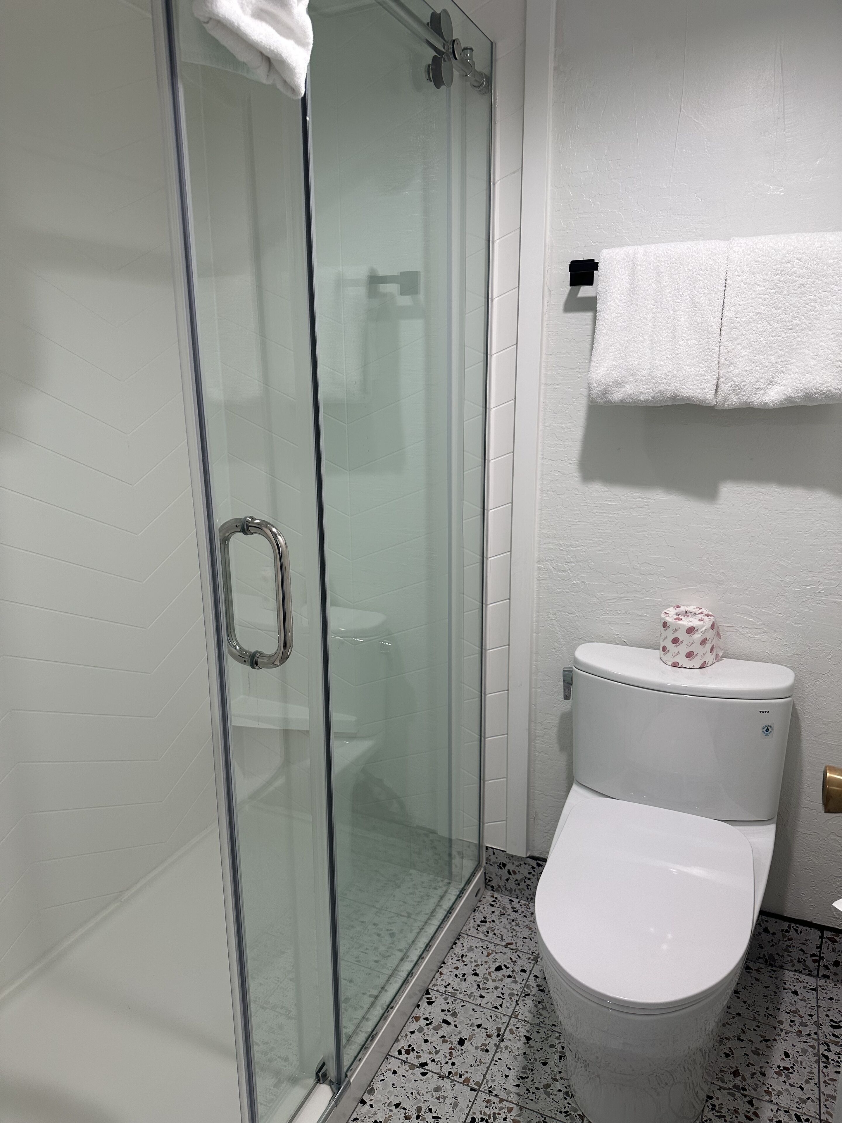 A bathroom with a glass shower enclosure, a toilet, and a towel rack with a towel.