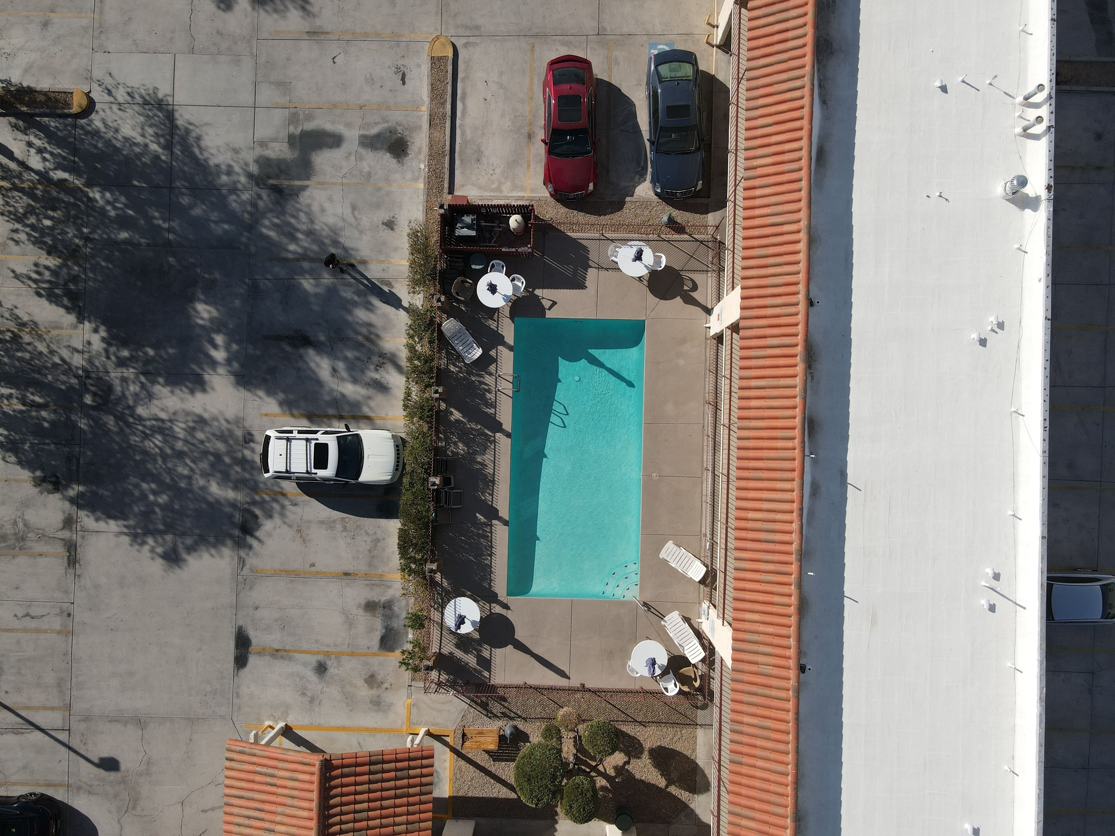 Vista aérea de um estacionamento com piscina, dois carros e área de estar ao ar livre.
