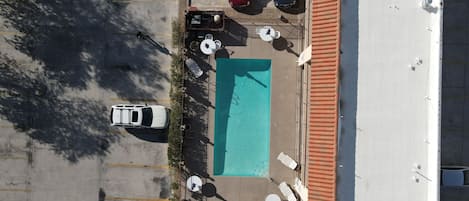 Vista aérea de um estacionamento com piscina, dois carros e área de estar ao ar livre.