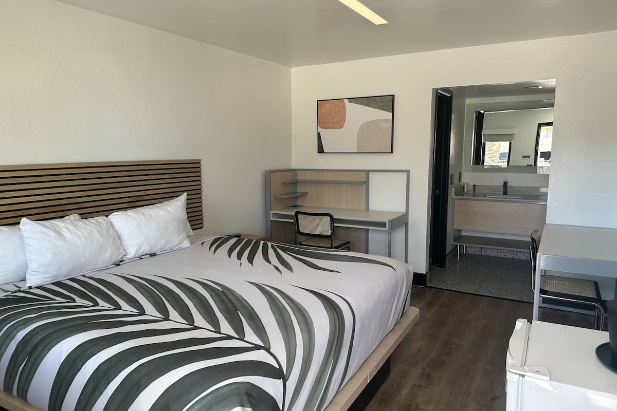 Una camera d'albergo moderna con un letto grande, una scrivania e un bagno visibile attraverso una porta aperta.