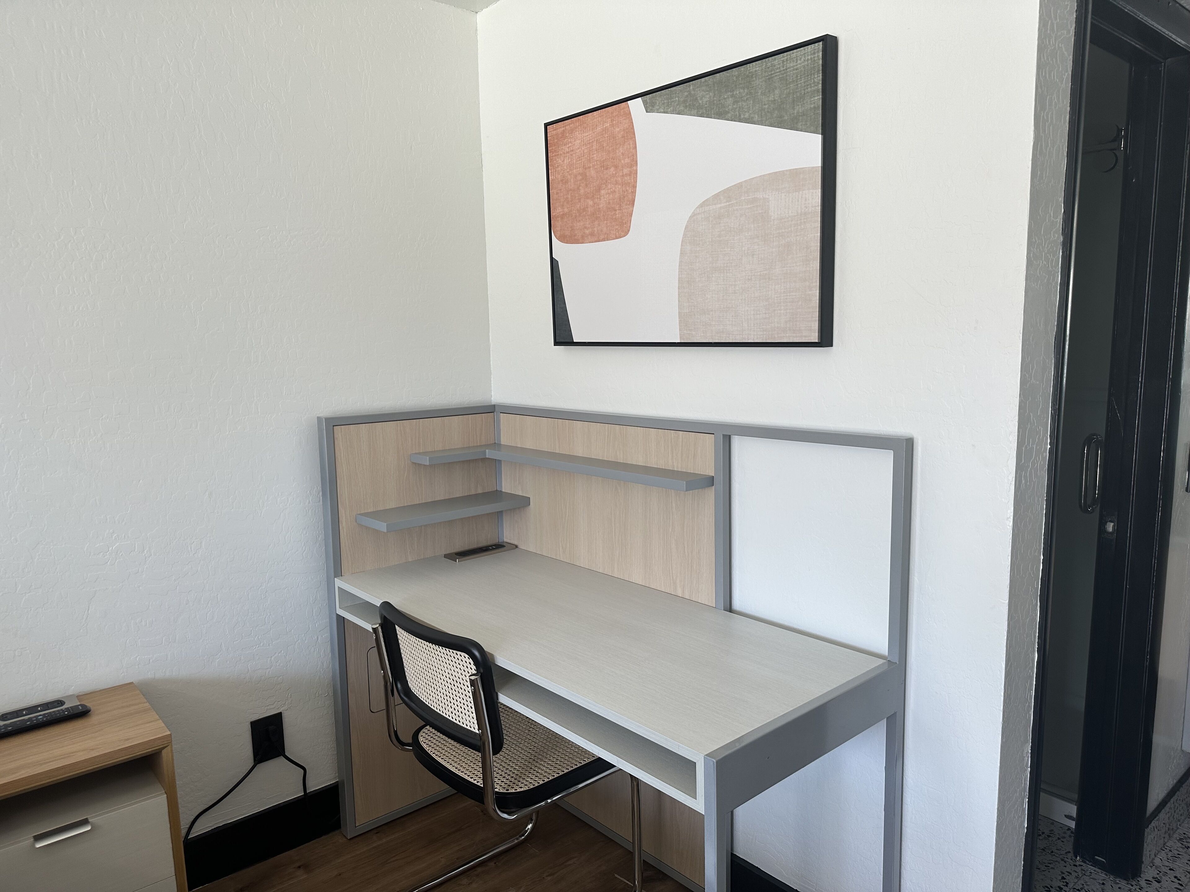 A compact, modern workspace with a desk, chair, and a mounted abstract painting.