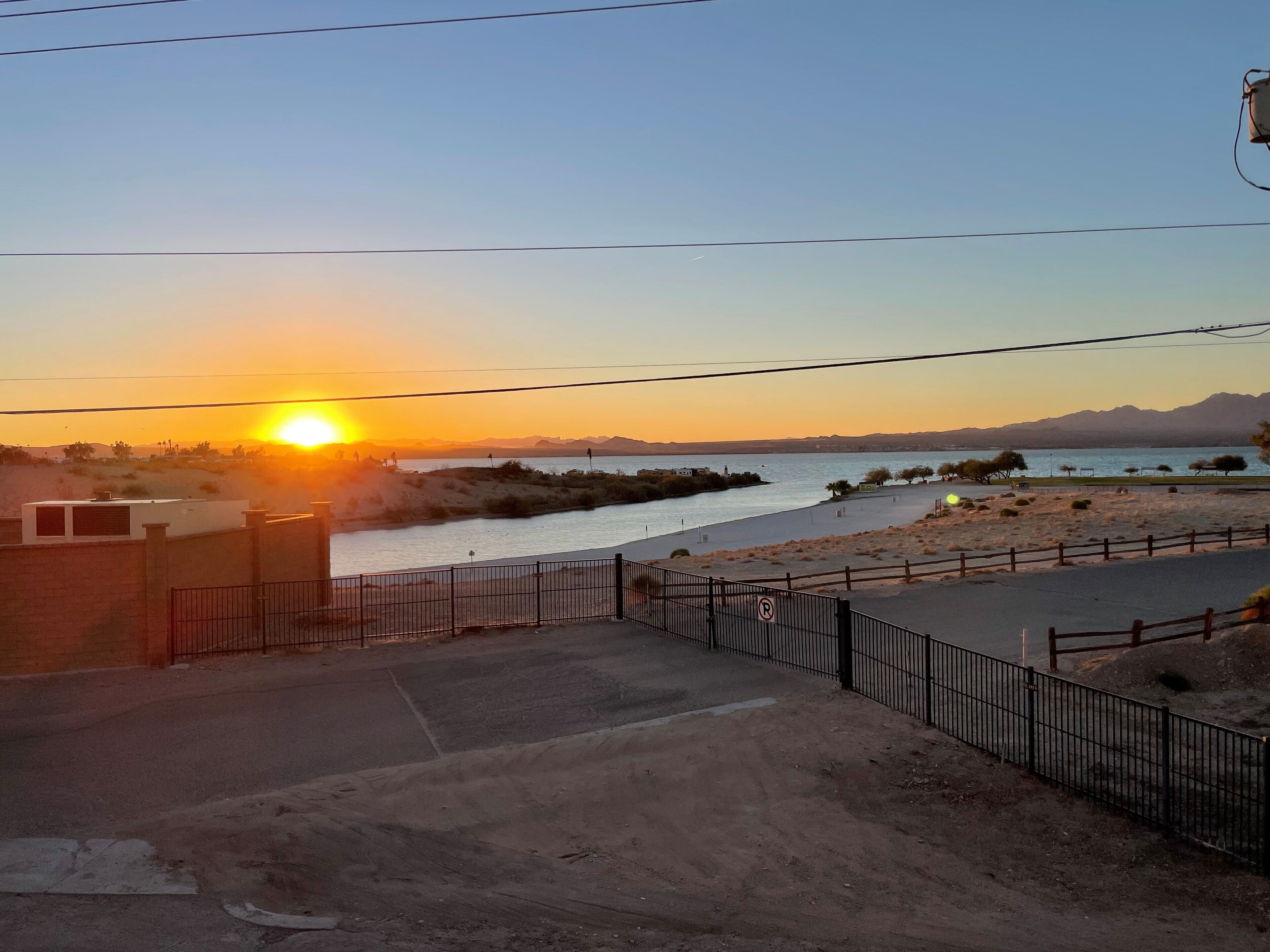 Une vue sur un coucher de soleil au-dessus d’une rivière, avec une plage de sable et une clôture au premier plan.
