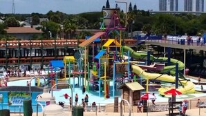 A water park with multiple slides and pools, surrounded by buildings and palm trees.