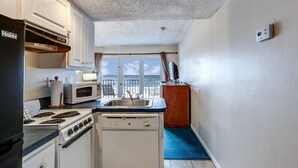A compact kitchen with a stove, microwave, and dishwasher. A window with curtains leads to a balcony.