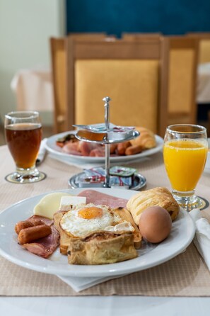 A breakfast setting with toast, eggs, sausages, ham, and a drink. - Four Seasons Hotel (Glyfada)