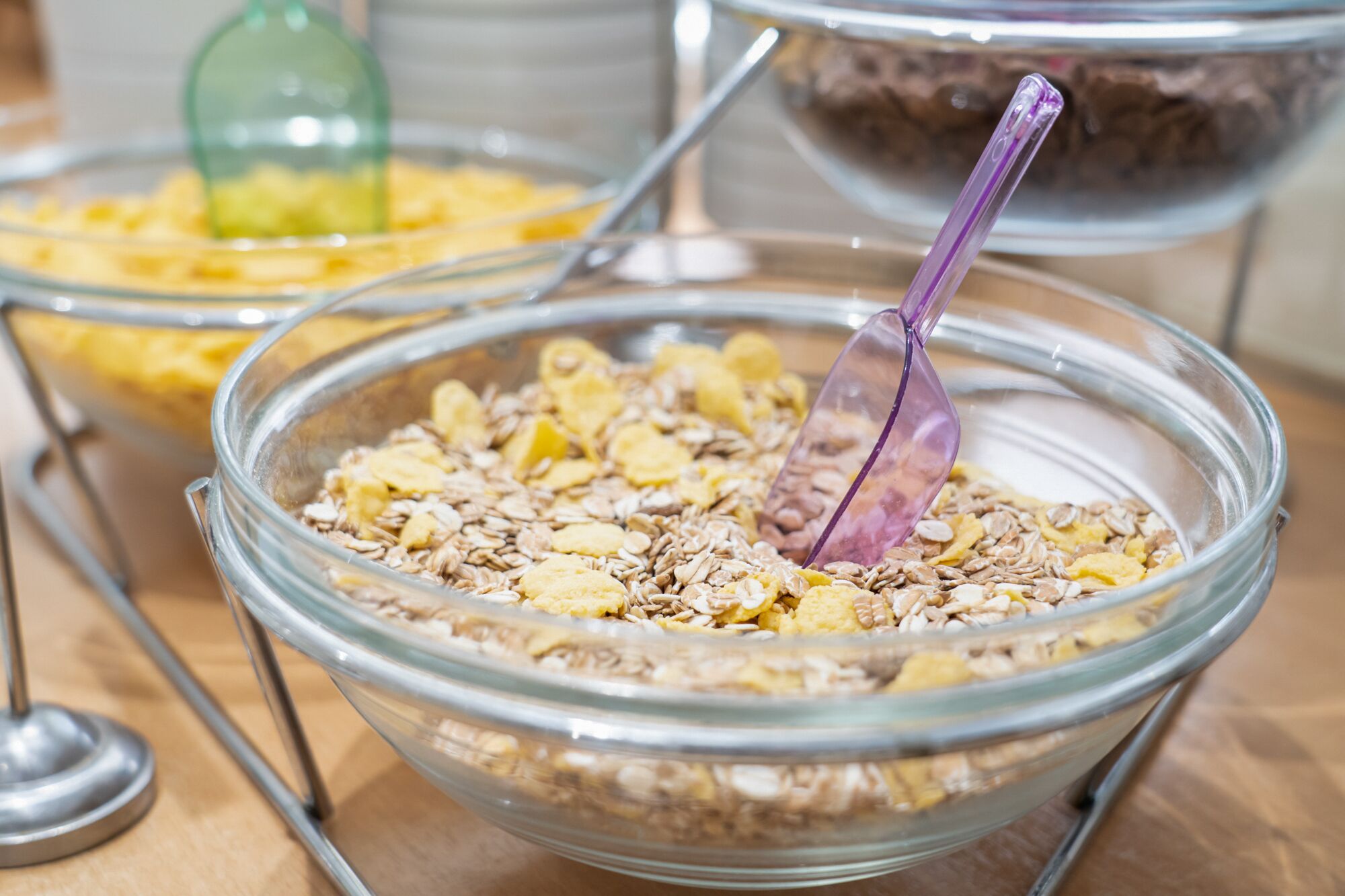 Un bufé con diversos alimentos en recipientes de vidrio transparente, incluyendo avena y otros cereales.
