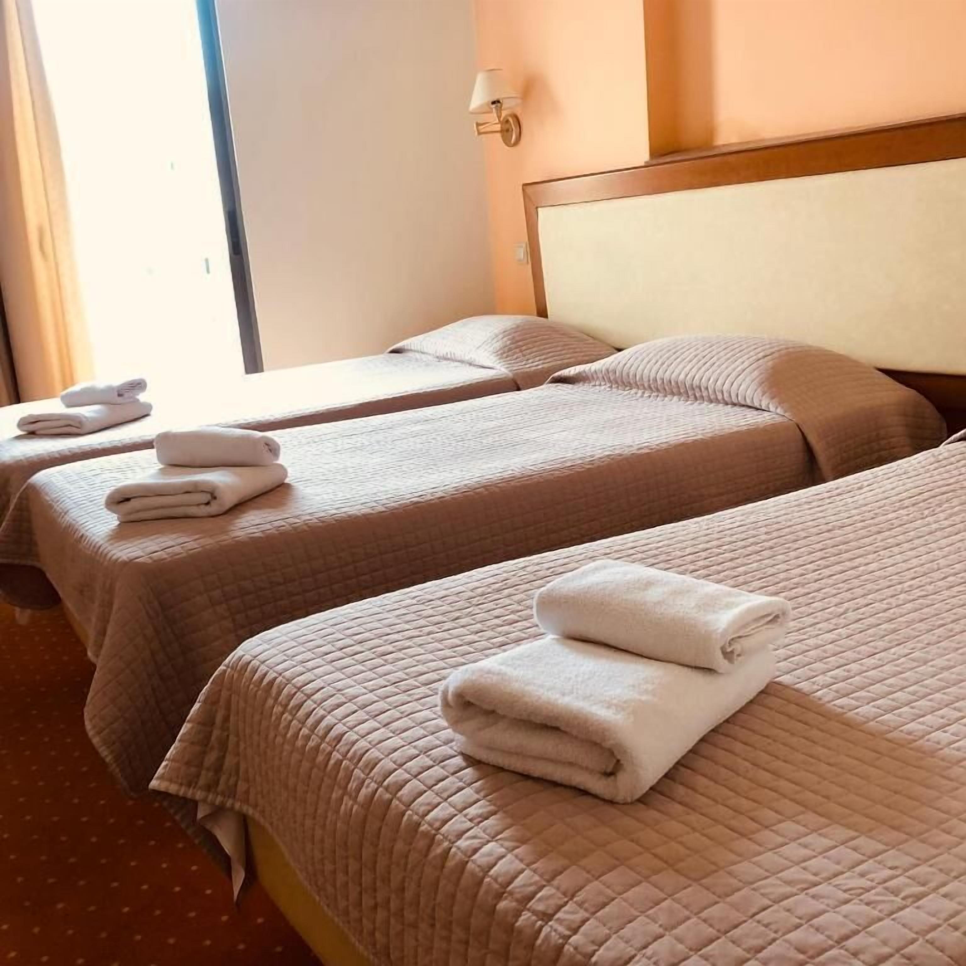 Una habitación de hotel con dos camas individuales, cada una con una toalla blanca doblada con cuidado.