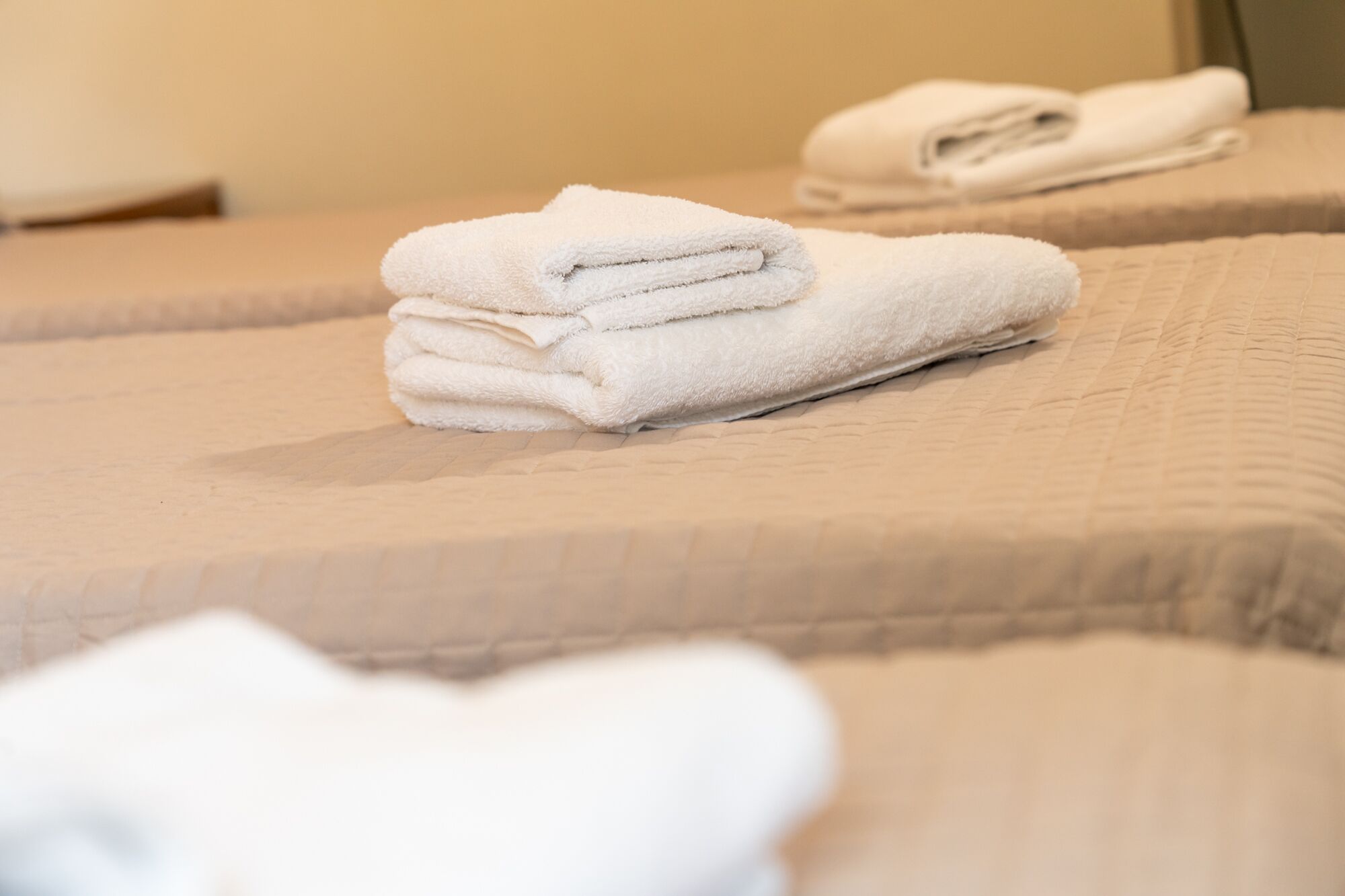 A set of neatly folded white towels stacked on a beige bed with a textured cover.