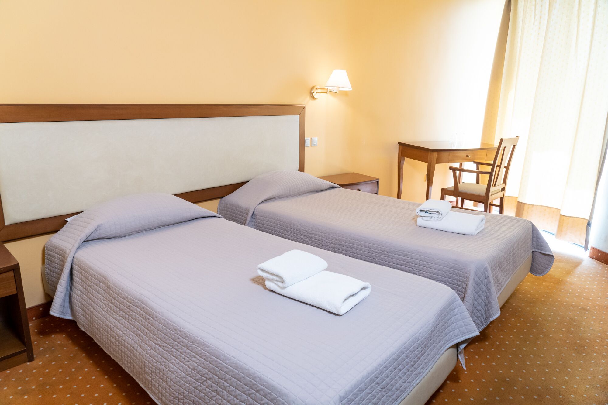 A hotel room with two beds, a desk, a chair, and a nightstand.