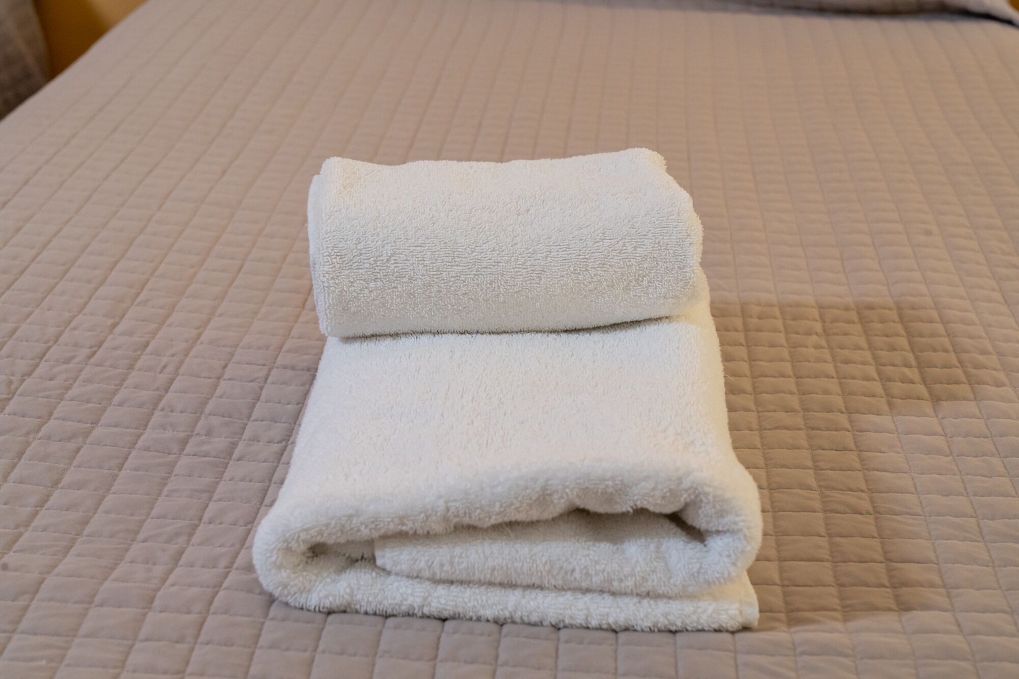Una toalla blanca doblada con cuidado sobre una cama con cubrecama acolchado.
