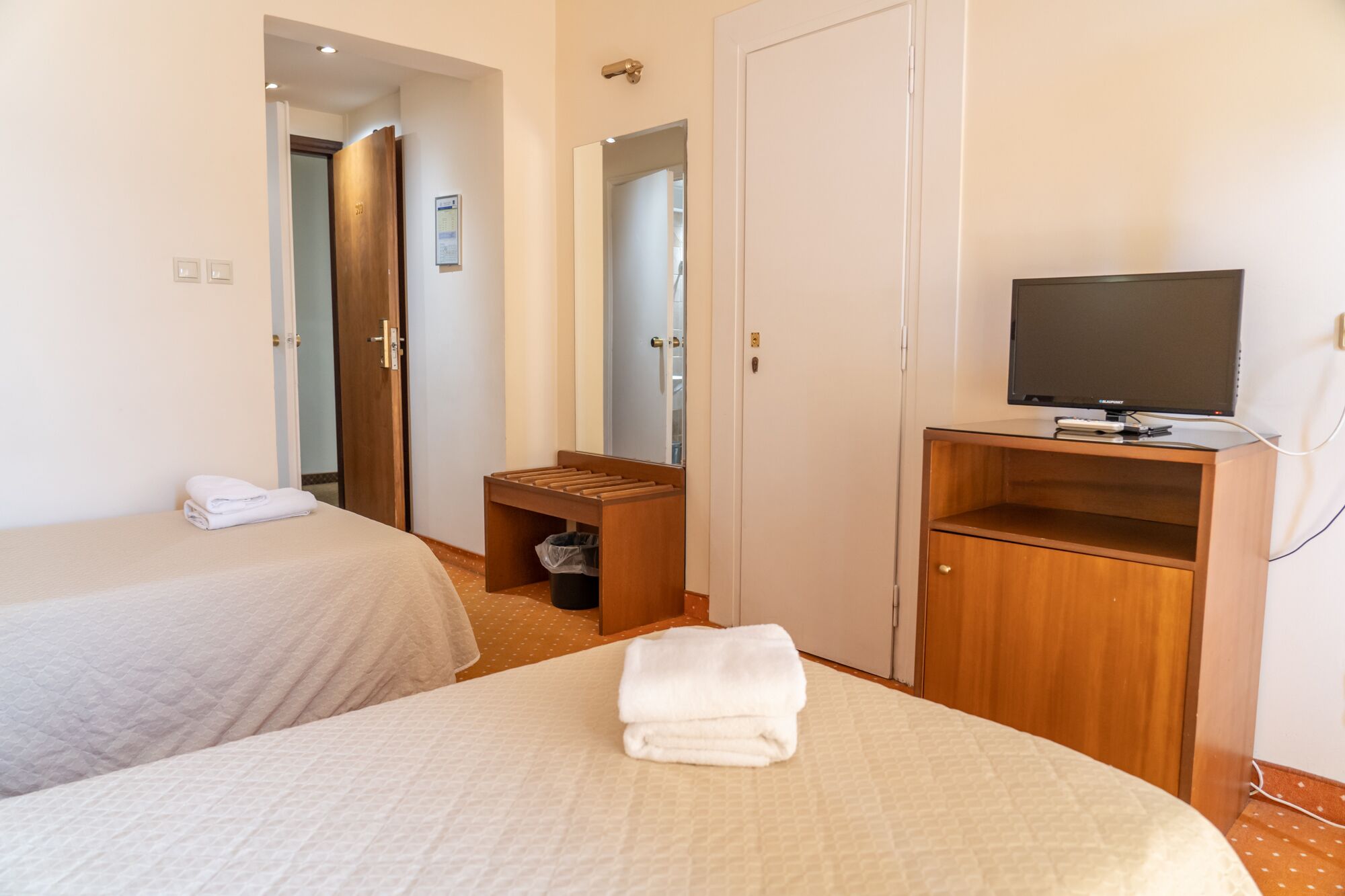A hotel room with two beds, a television on a wooden stand, and a bathroom visible through an open door.