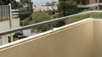 A balcony with a small table and a chair, overlooking a beach and a body of water.