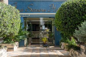 The entrance of a hotel with a blue facade and the name 'Four Seasons Hotel' in gold lettering. There are potted plants and a tiled pathway leading to the entrance. - Four Seasons Hotel (Glyfada)