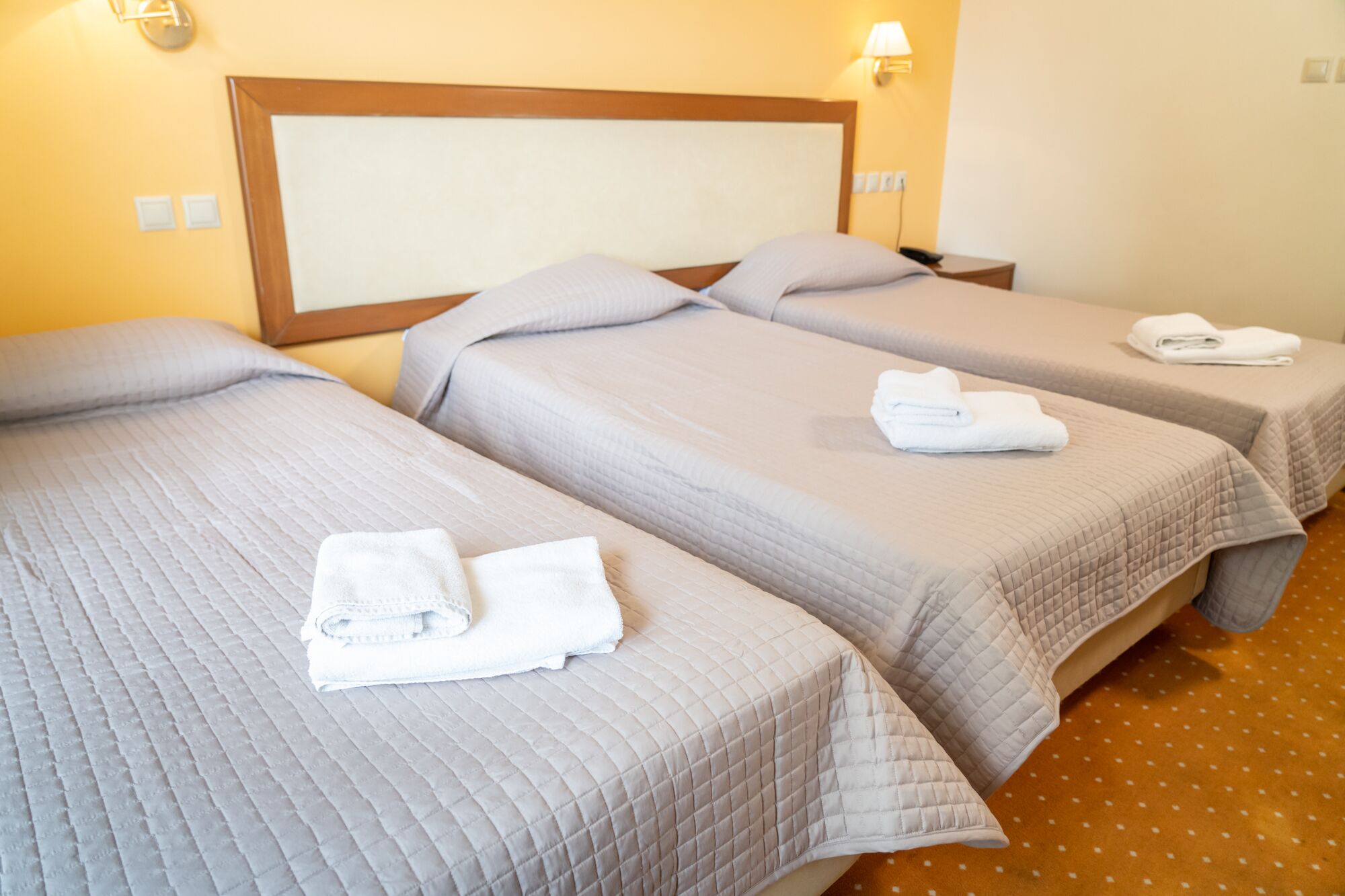A hotel room with two beds, each with a quilted bedspread and pillows, and a headboard. There are white towels on each bed.