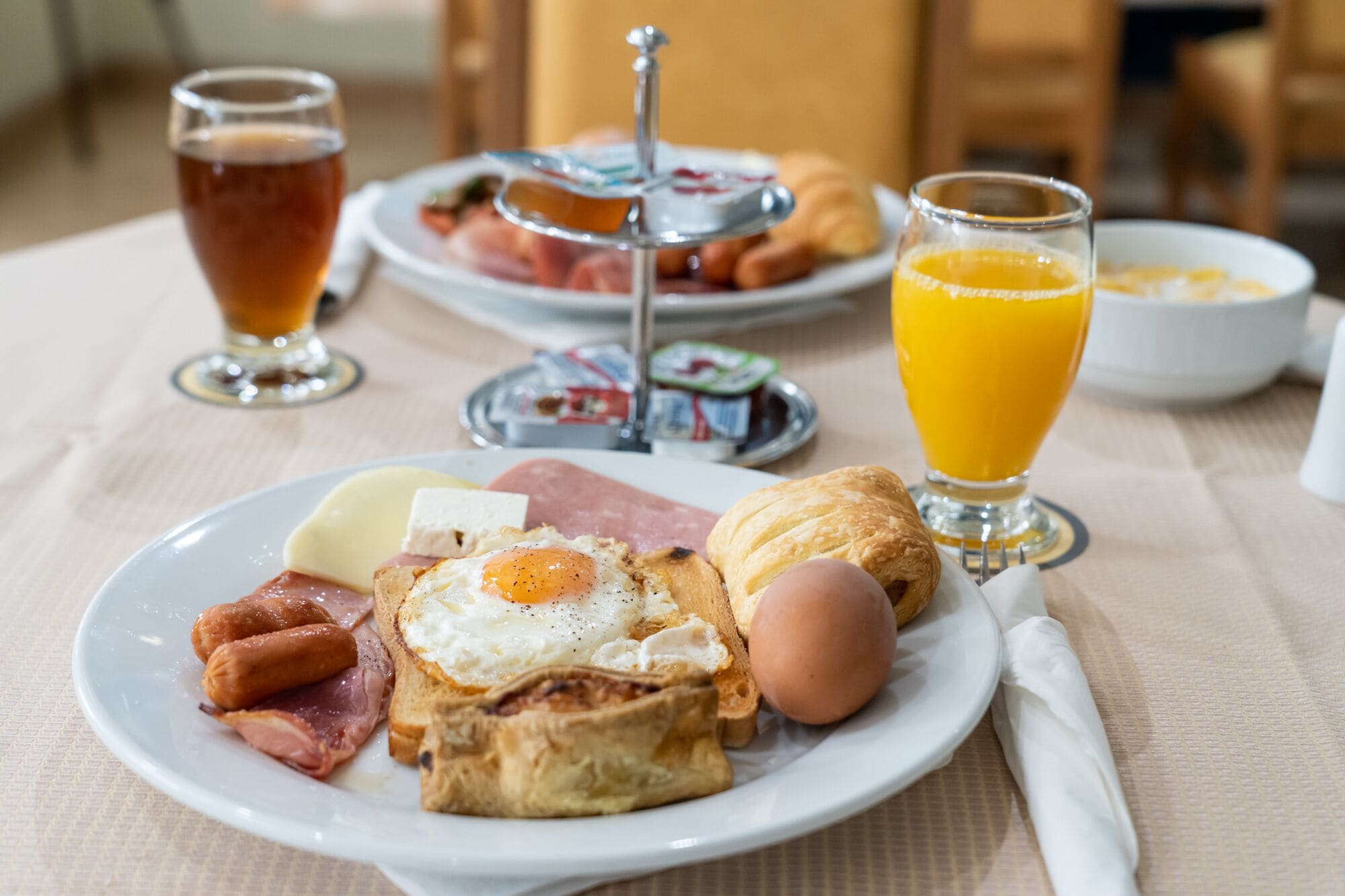 A breakfast plate with eggs, ham, cheese, and toast, accompanied by a glass of orange juice and a glass of tea.