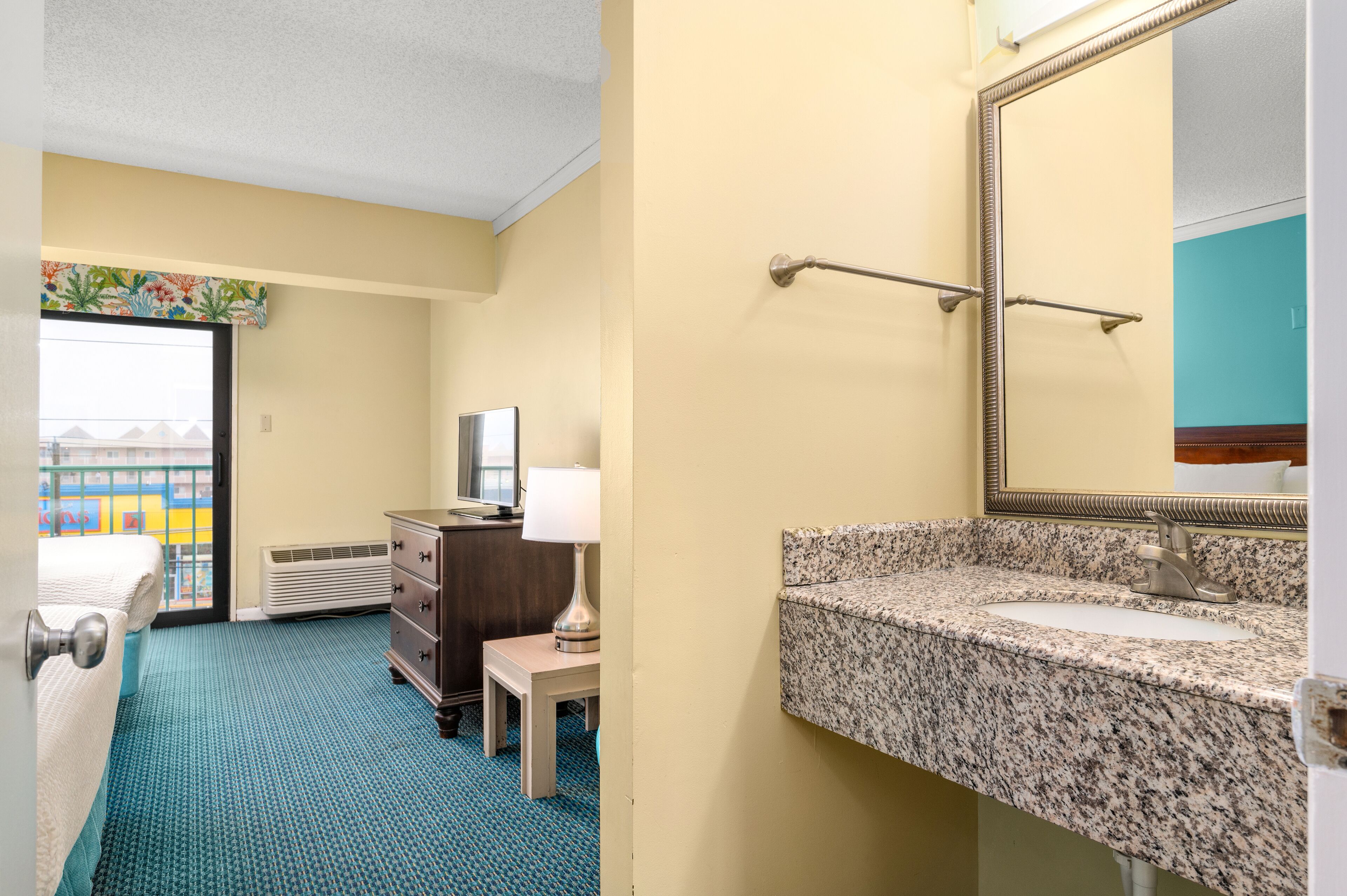 Hotelkamer met een bed, een kaptafel, een lamp en een badkamer met een granieten aanrechtblad en een spiegel.