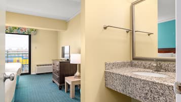 A hotel room with a bed, dresser, lamp, and a bathroom with a granite countertop and mirror.