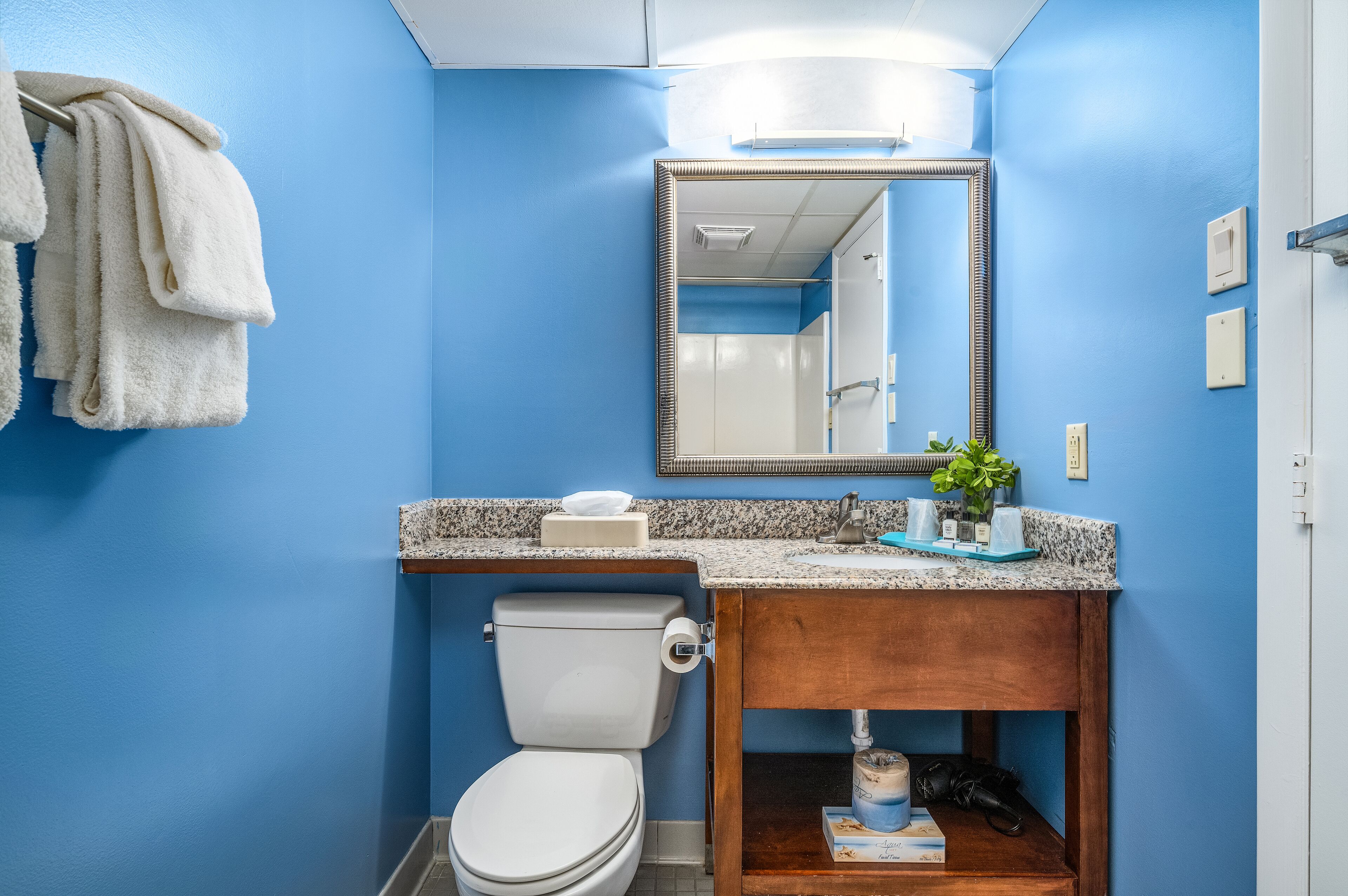 Een badkamer met een blauwe wand, een wit toilet, een granieten aanrecht en een spiegel boven de wasbak.
