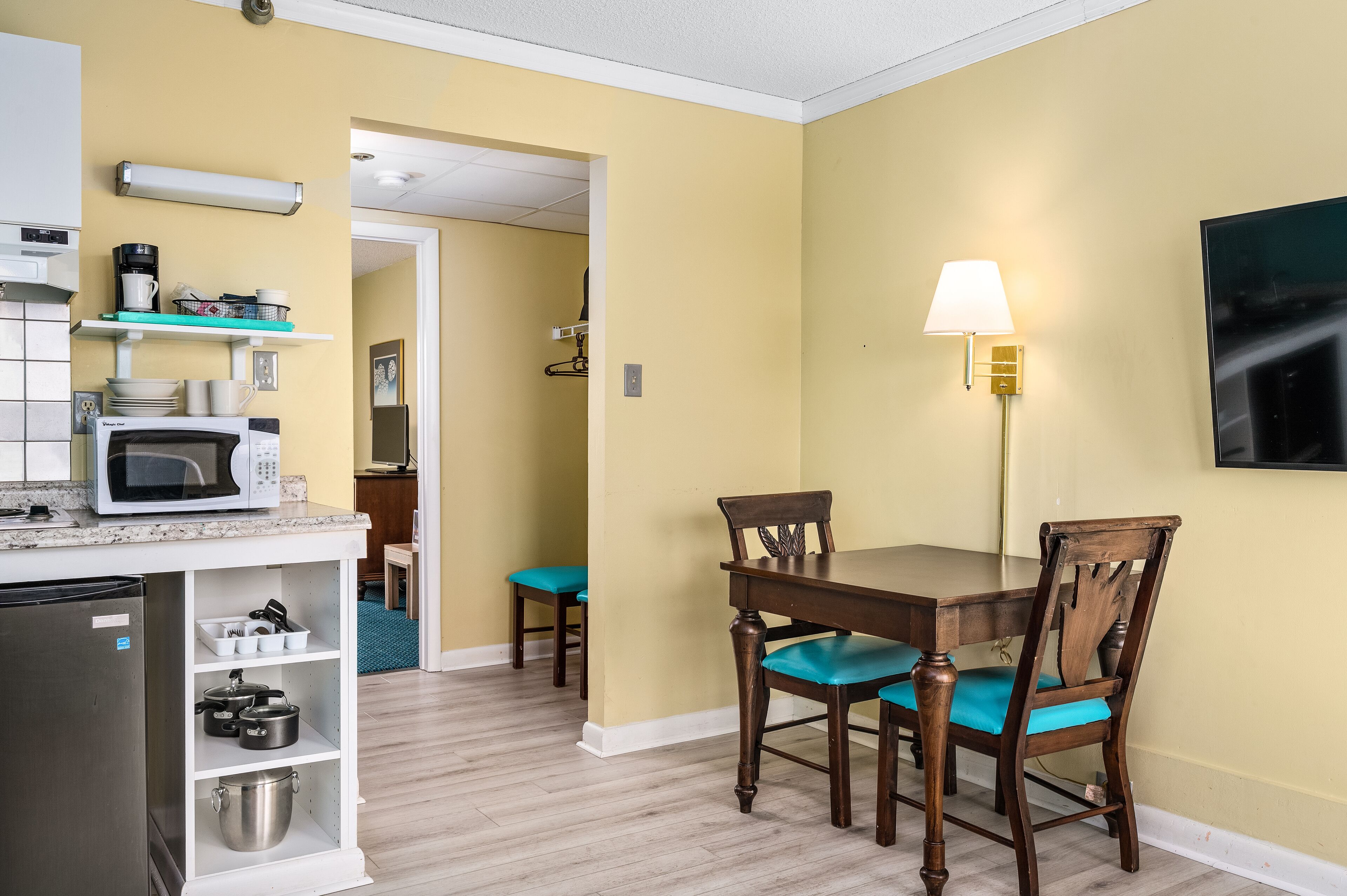 A compact kitchen with a microwave, coffee maker, and shelves with dishes and pots.