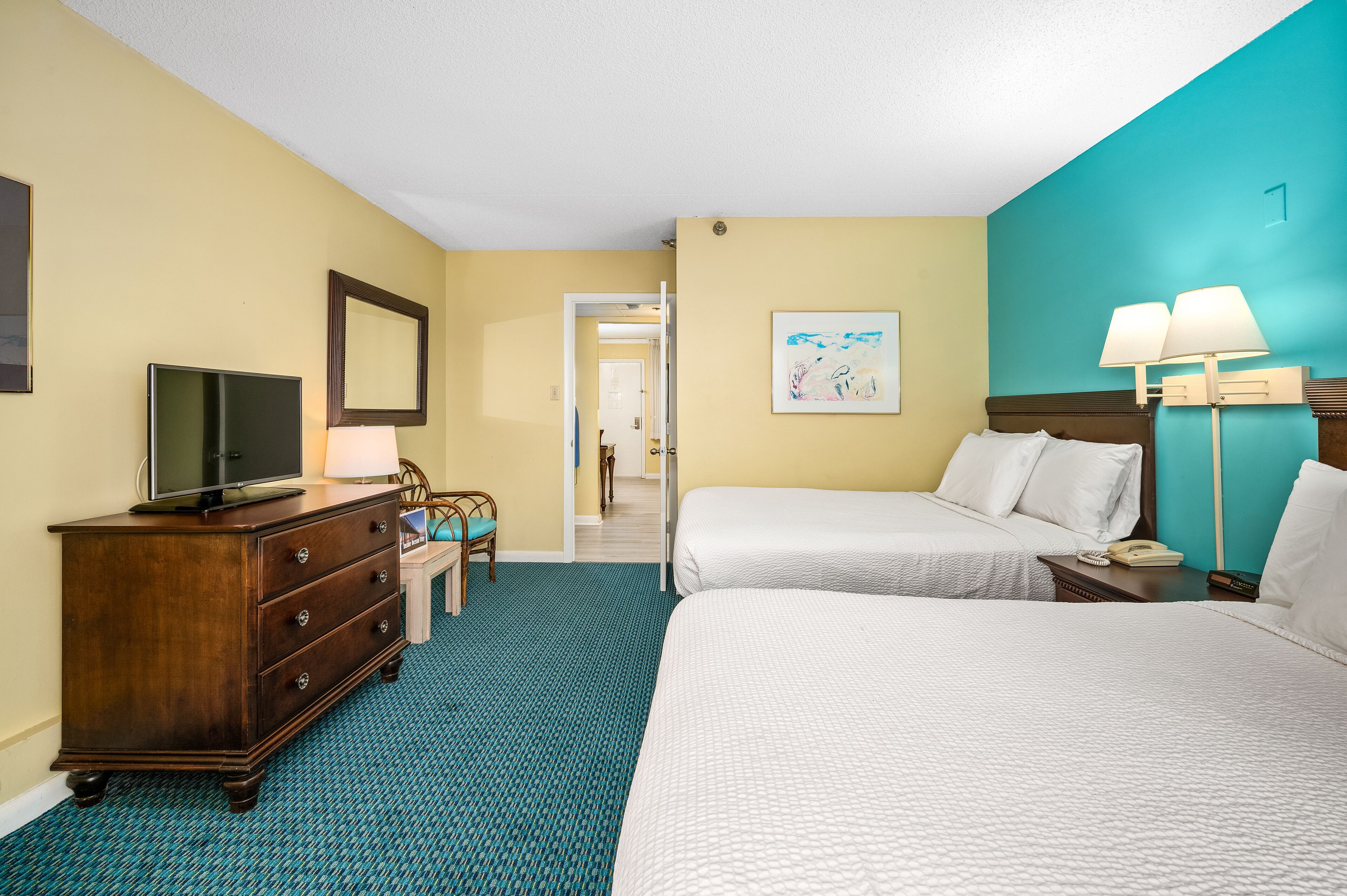 A hotel room with two beds, a TV, a dresser, and a desk with a lamp.