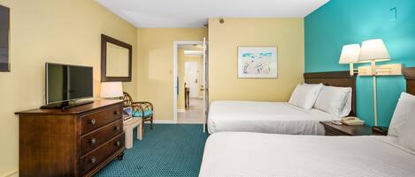 A hotel room with two beds, a TV, a dresser, and a desk with a lamp.