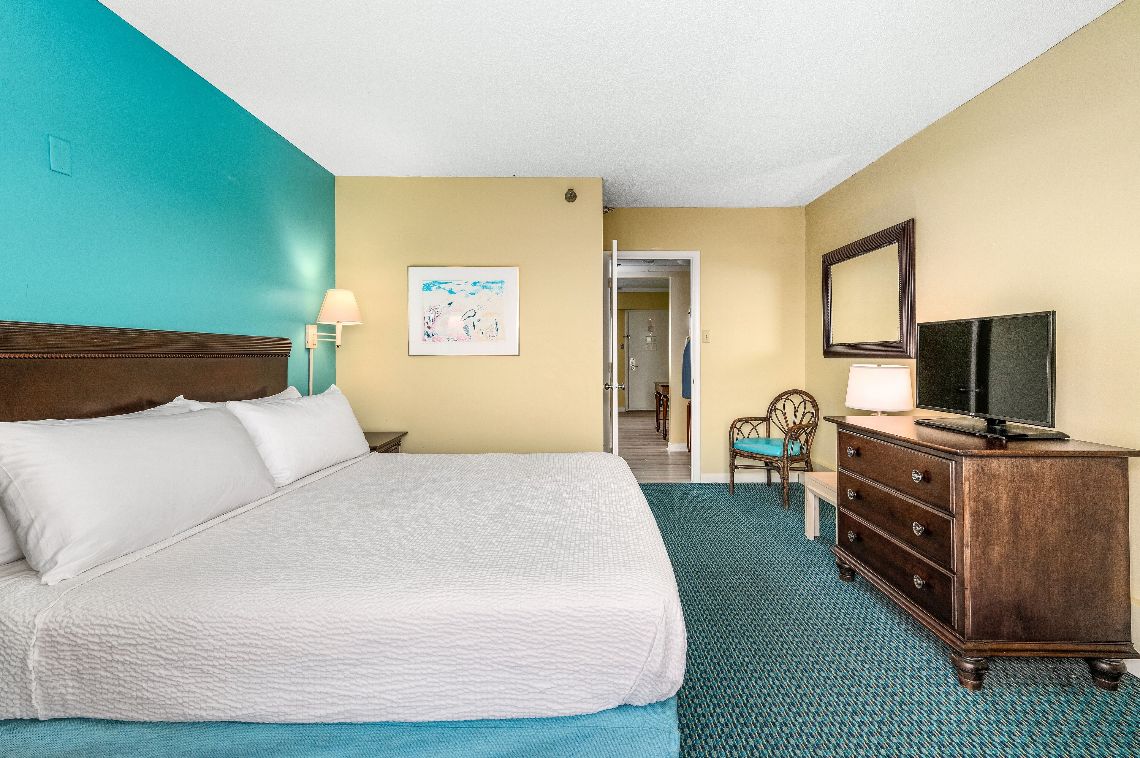 Quarto de hotel com cama, penteadeira, televisão e um quadro na parede.